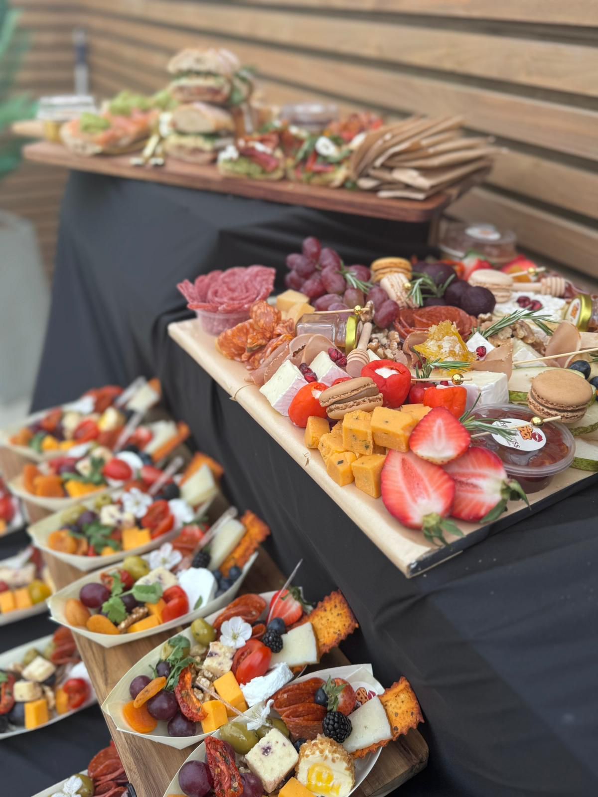 Tiered display of grazing boards and individual cones with sandwiches in the background