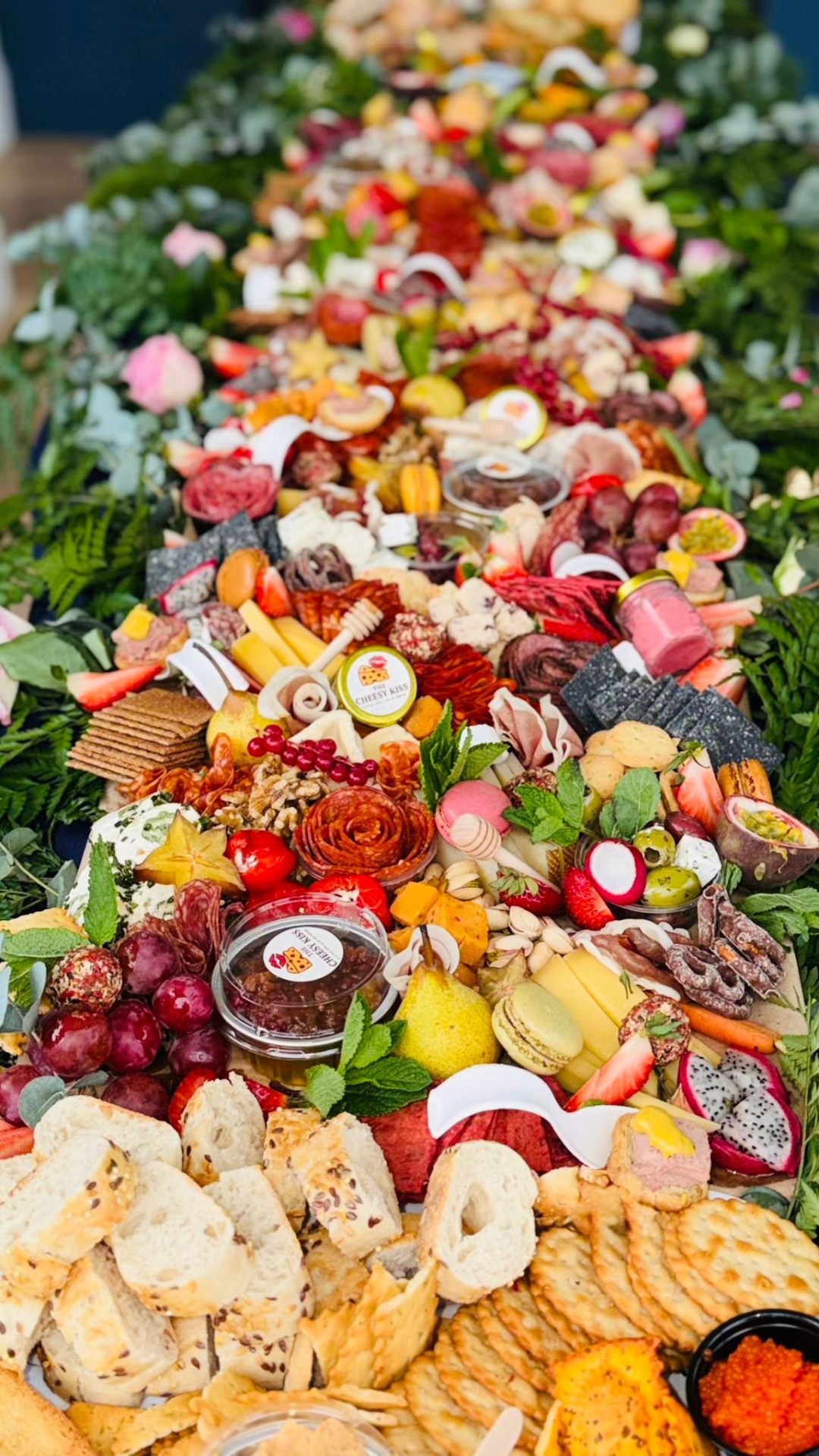 Close-up of charcuterie roses, soft cheeses, macarons and fresh fruit on a floral grazing table